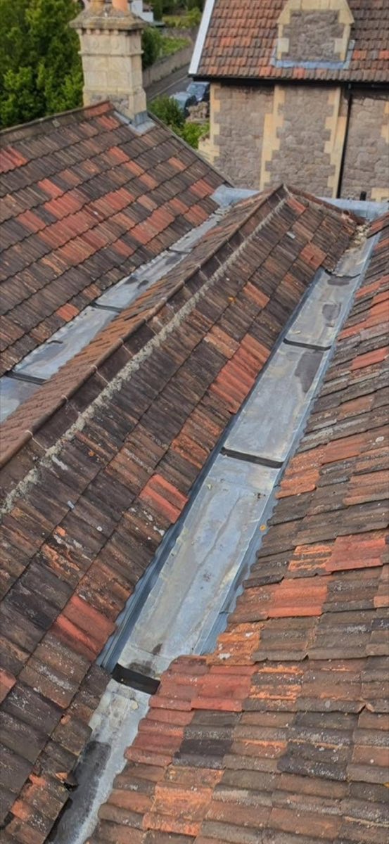 Drone view looking down a roof valley between two pitched clay-tiled roofs with lead flashing
