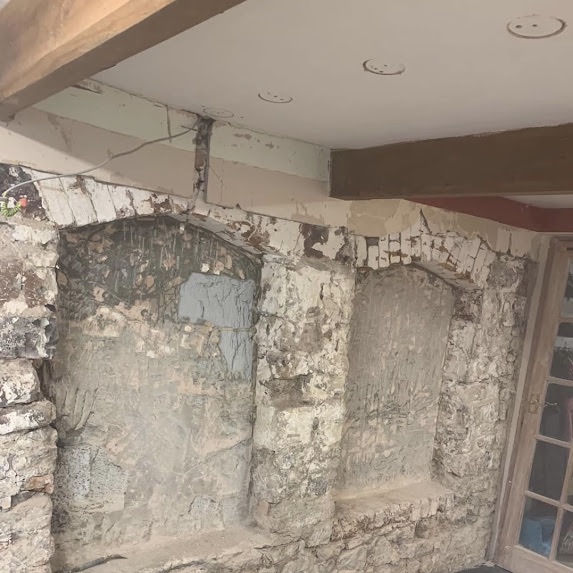 A rubble-stone wall taken back to bare stone, with two arched recesses roughed out and old damp staining across it