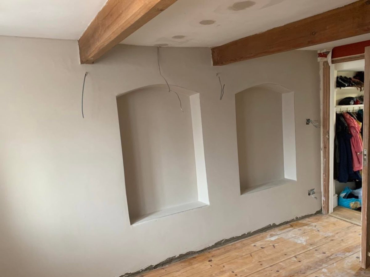 The finished wall, with two smooth hand-formed curved niches, exposed timber beams and bare floorboards