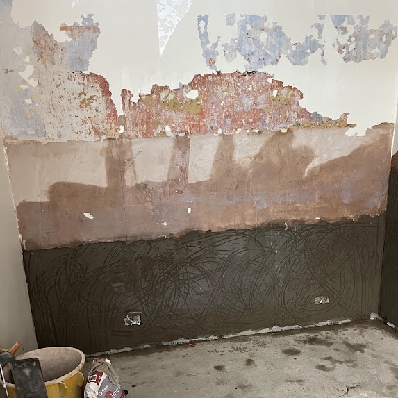 The lower half of a wall covered in a dark render scratch coat with a heavy swirled key pattern for the next coat to grip
