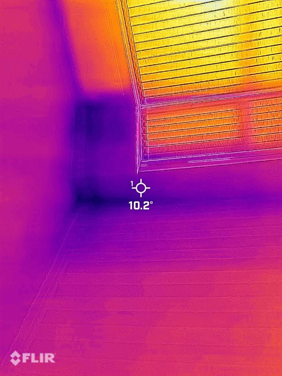 A FLIR thermal image of a room corner showing a cold, damp area